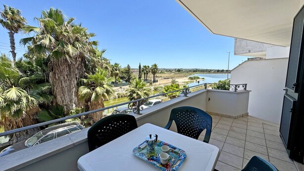 Een balkon met een tafel en stoelen, met uitzicht op een waterpartij en palmbomen.