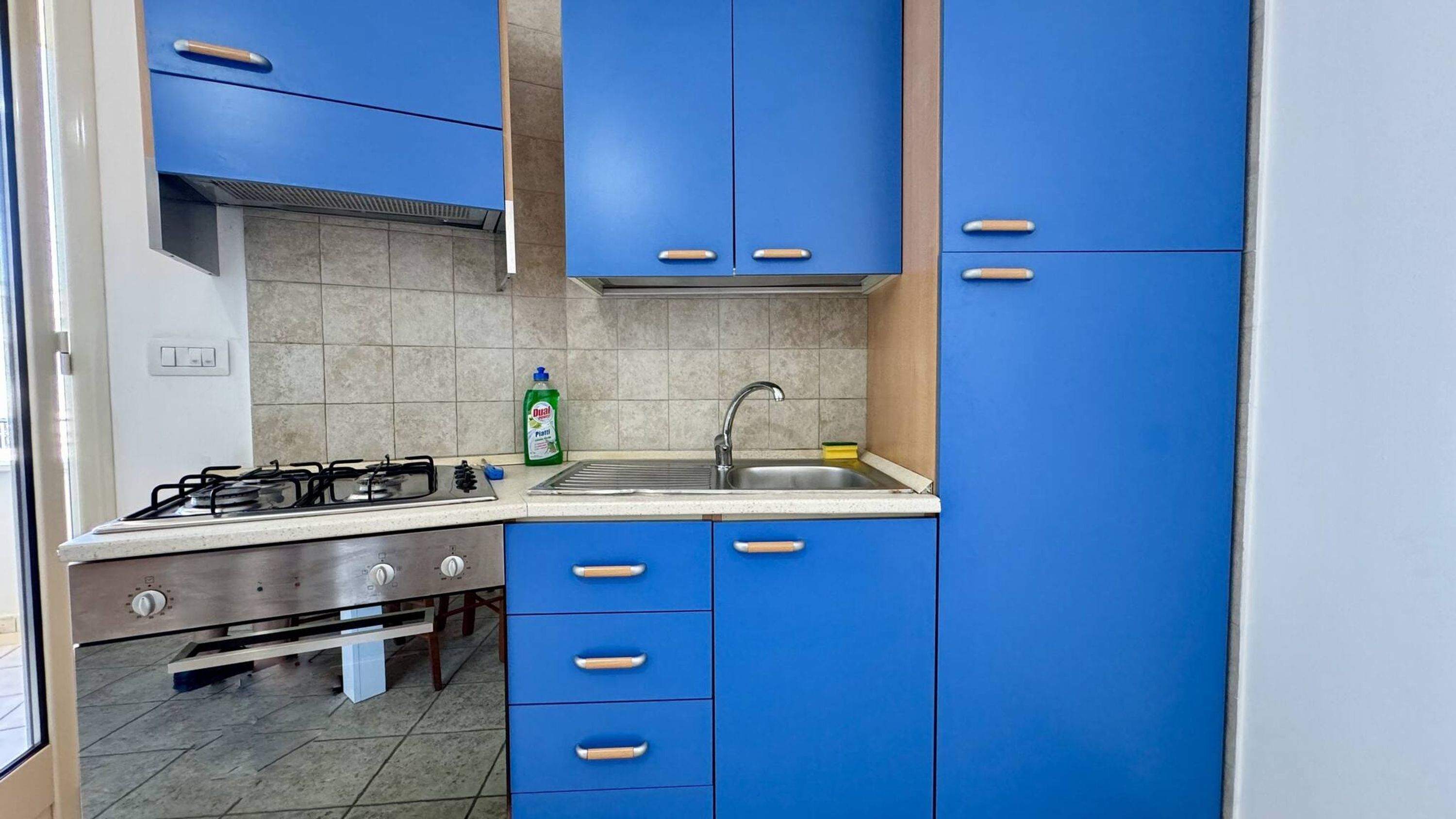 A kitchen with blue cabinets, a gas stove, a sink, and a dish soap bottle.