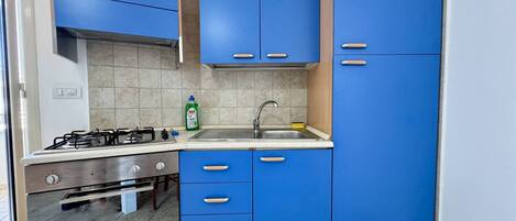 A kitchen with blue cabinets, a gas stove, a sink, and a dish soap bottle.