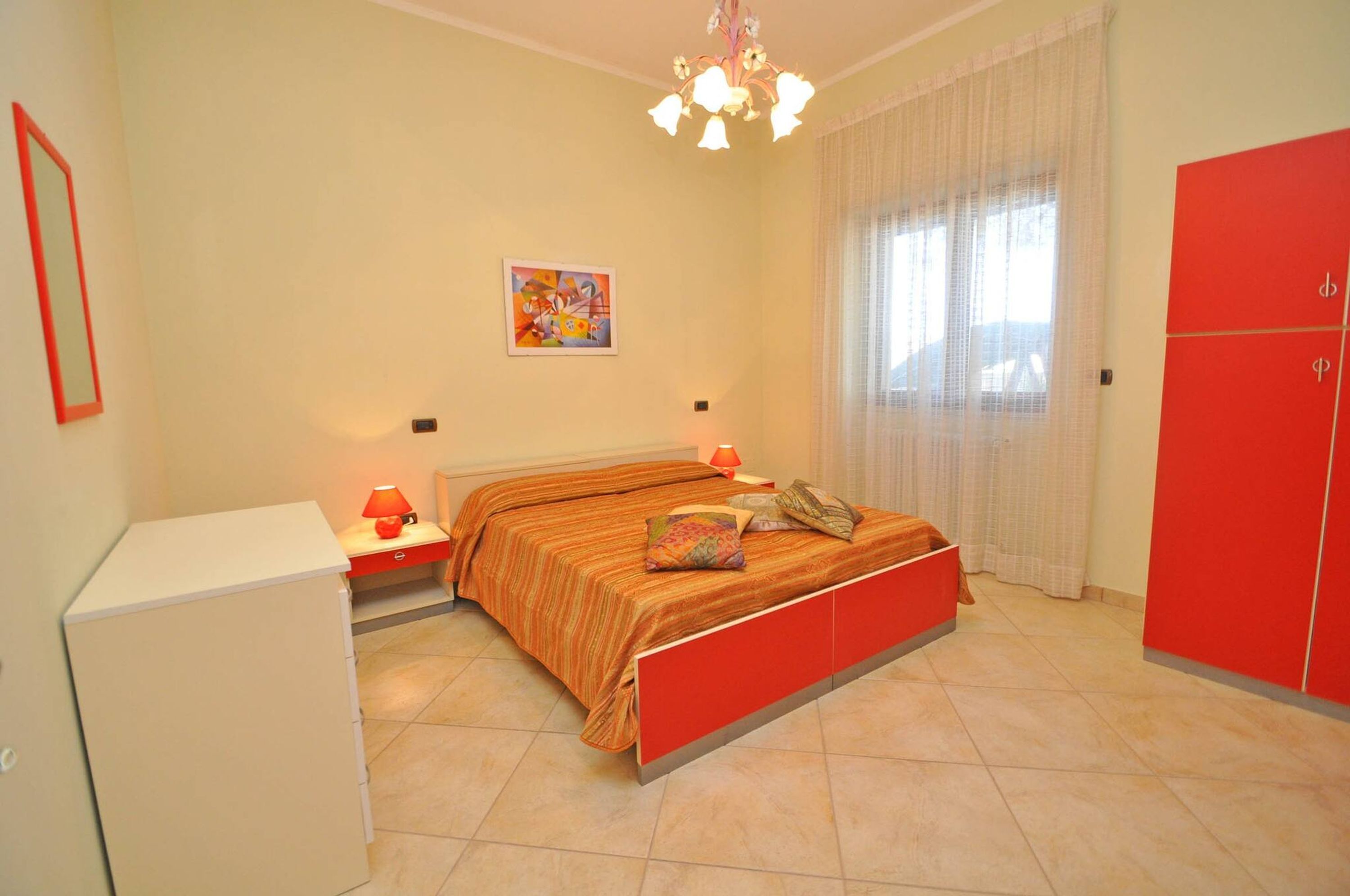 A bedroom with a bed, a nightstand, a lamp, a wardrobe, and a painting on the wall.