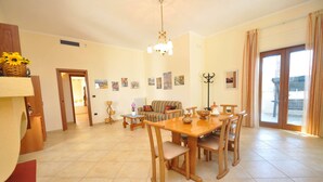 A spacious living area with a dining table, chairs, a sofa, and a chandelier. There are several framed pictures on the walls and a large window with curtains. - Villa Marechiaro 50 m From the sea 3 Bedrooms 2 Bathrooms (Racale)