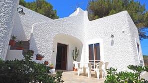 Un edificio de estuco blanco con un patio, plantas en macetas y un cactus.