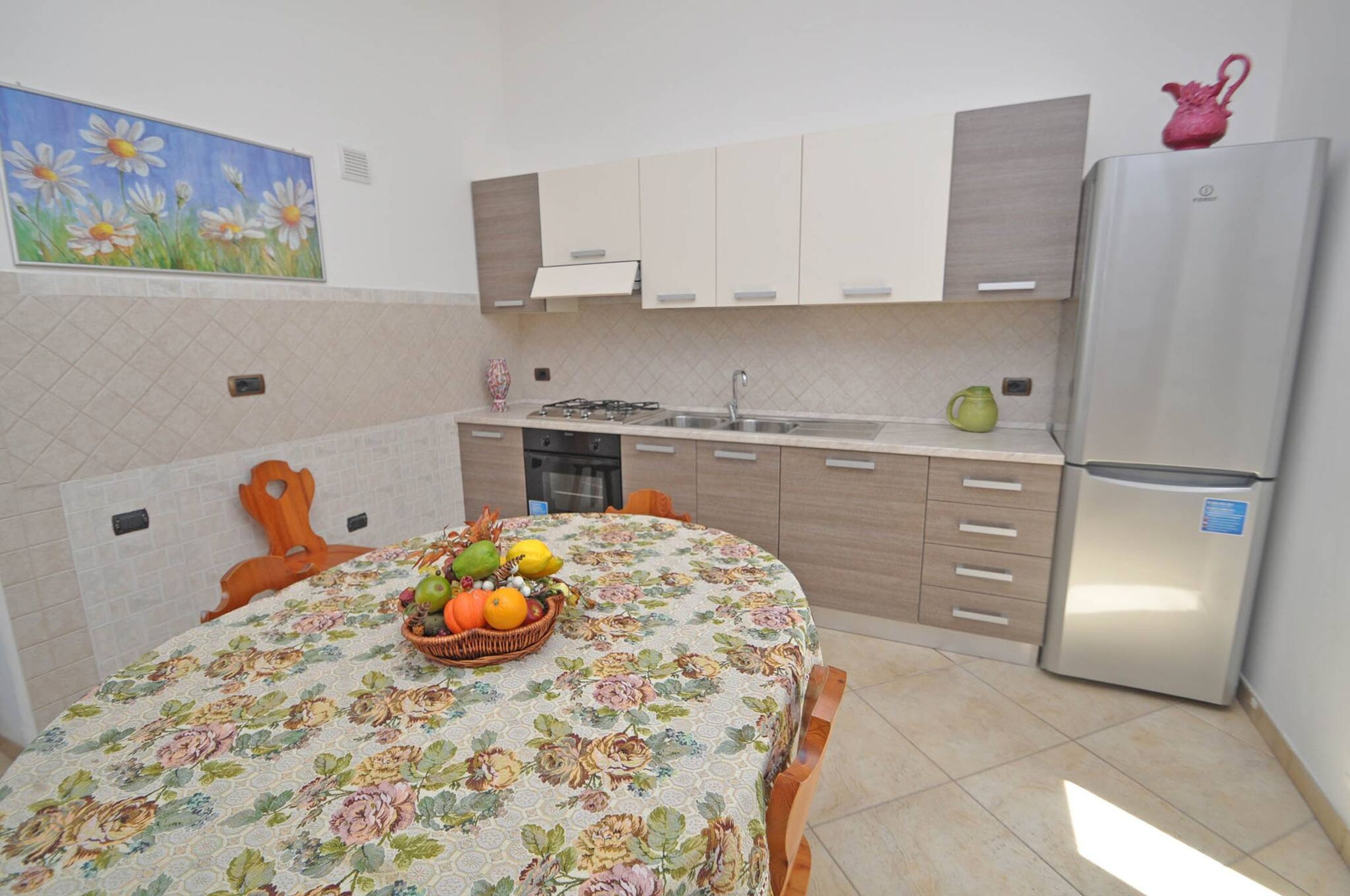 A kitchen with a dining table set, a refrigerator, and a painting on the wall.