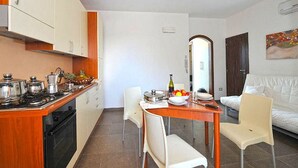 A compact kitchen with a dining area, white walls, and a sofa. - Bilocale Arainn 2 - Japigia (Ugento)
