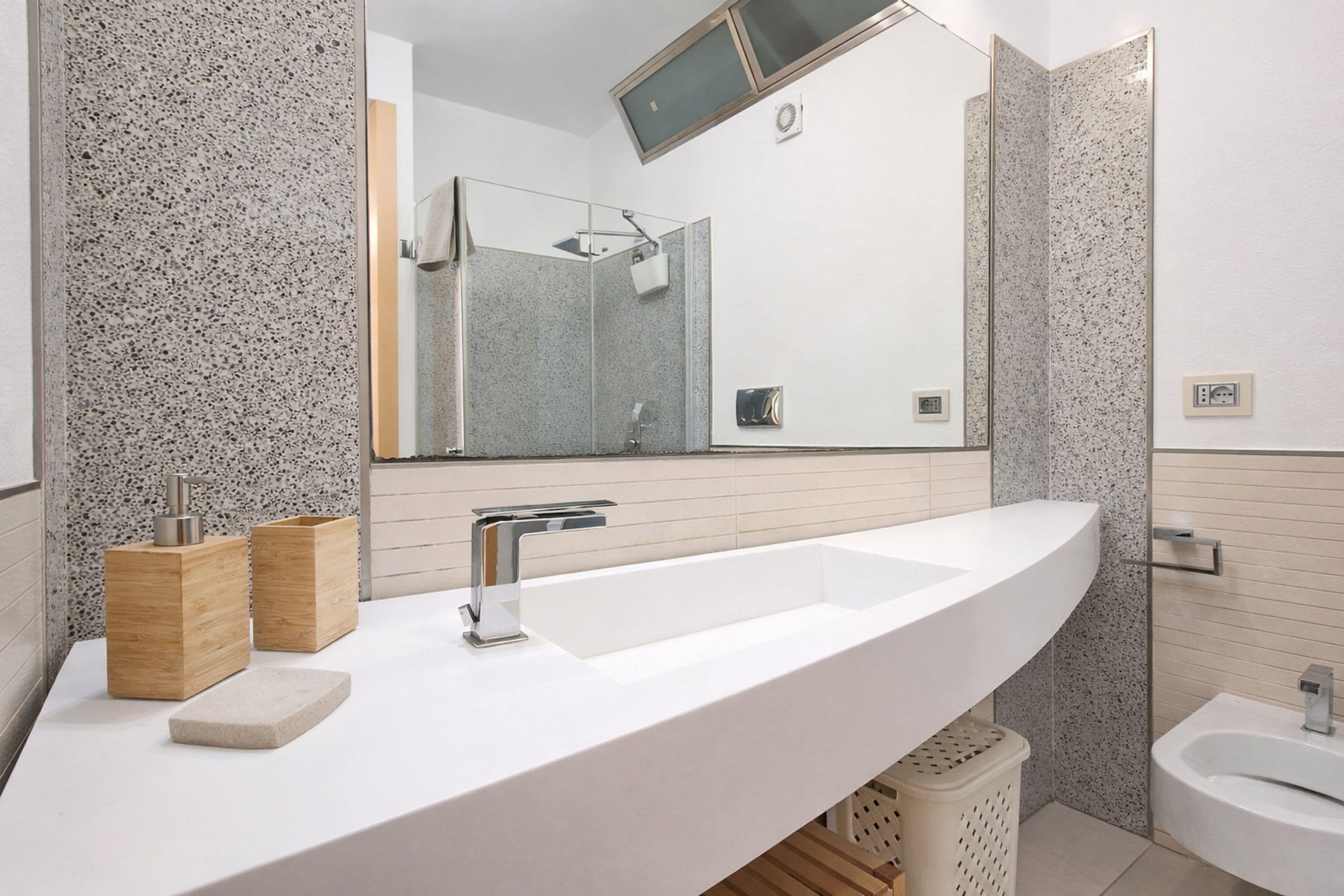 A modern bathroom with a large mirror, a white sink, and a shower area.