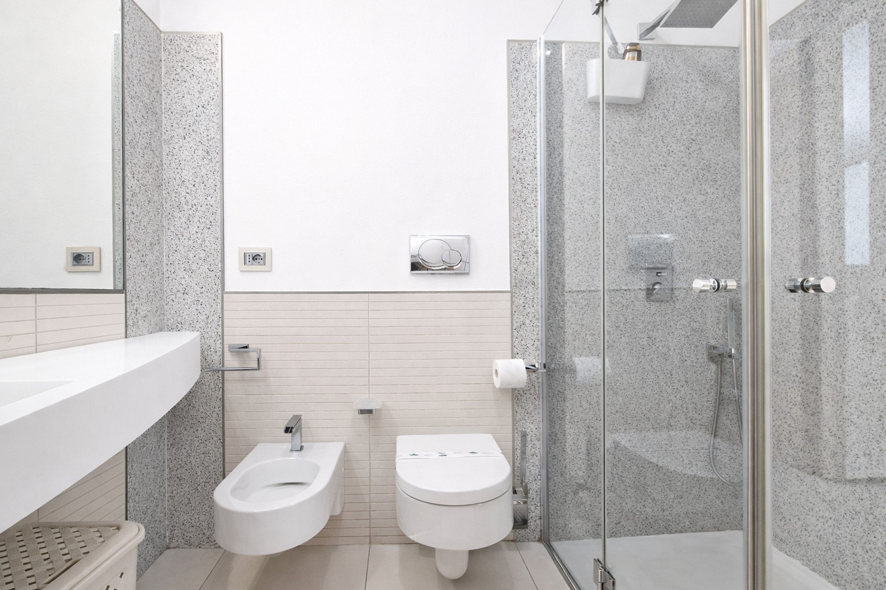 A modern bathroom with two toilets, a shower, and a glass-enclosed shower area.