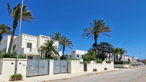 A residential area with modern white buildings, palm trees, and gated entrances. - Bilocale Arainn 1 - Lupiae (Ugento)