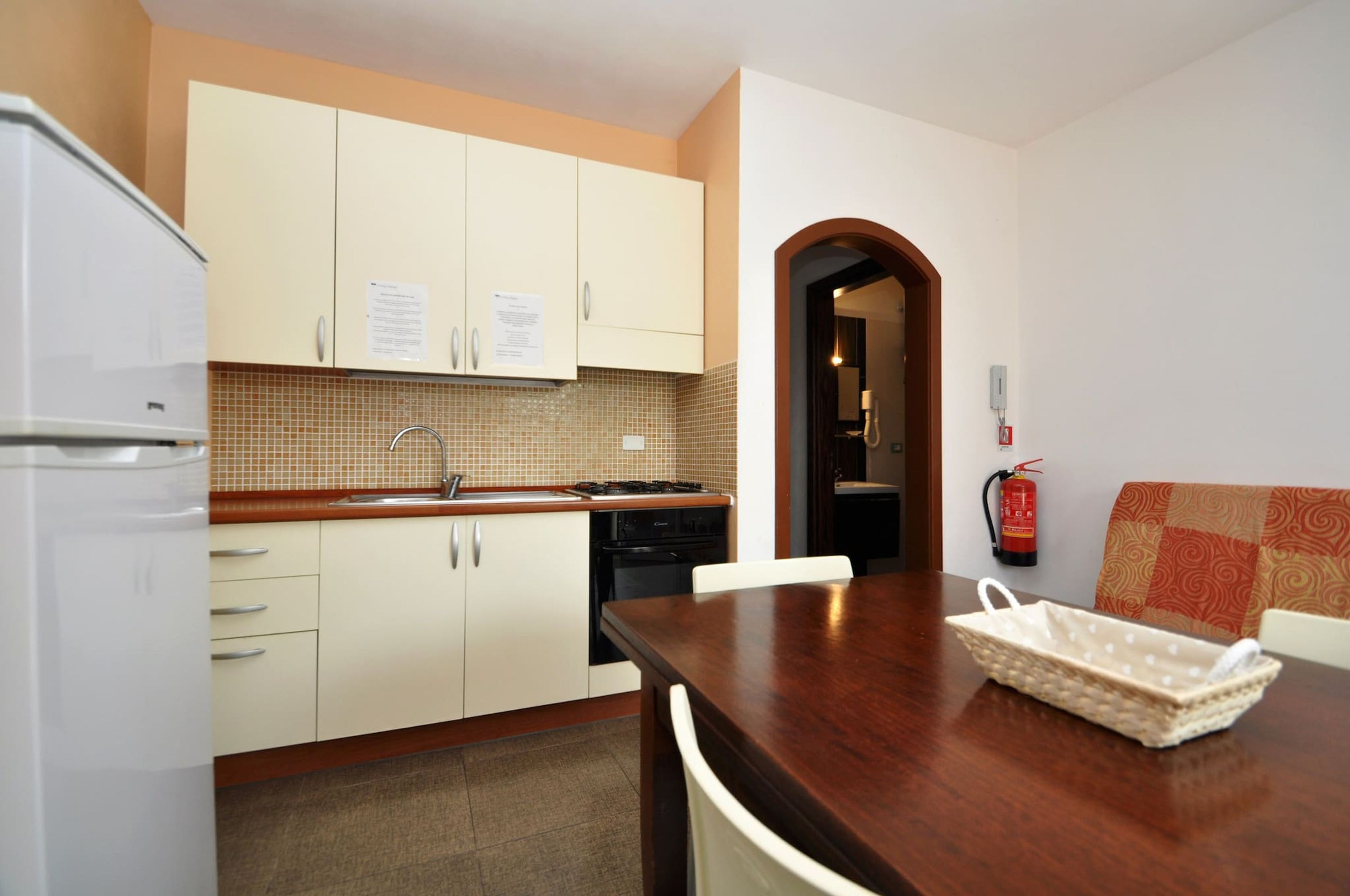 A compact kitchen with white cabinets, a wooden countertop, a stove, and a sink. There is a fire extinguisher mounted on the wall.