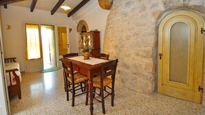 A dining area with a stone wall, wooden table, chairs, and a door with a glass panel. - Trullo Beneficati in Taviano (Taviano)