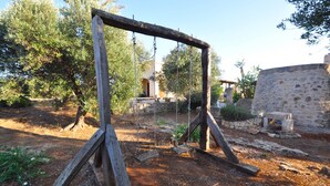 A rustic wooden swing set in a garden with stone walls and trees. - Trullo Beneficati in Taviano (Taviano)
