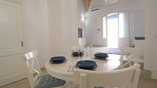 A dining area with a round table set for four, white chairs, and a view of a hallway with a door and a window. - Corte Nizza in Taviano (Taviano)