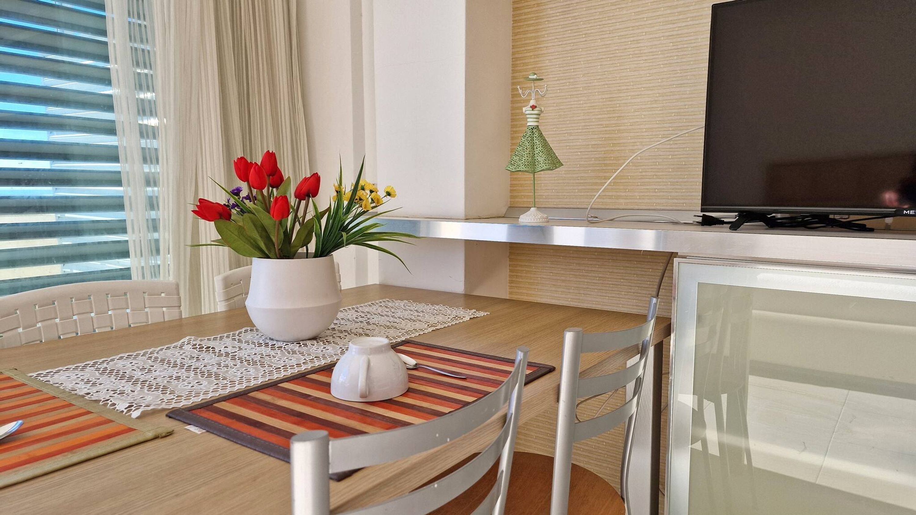 A modern dining area with a wooden table, white chairs, a vase of red tulips, and a decorative lamp.