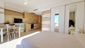 Ein modernes Hotelzimmer mit einem großen Bett, einem Essbereich mit Tisch und Stühlen, einer Küchenzeile und einem großen Spiegel, der den Raum reflektiert.