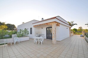Une maison blanche avec une terrasse carrelée, un espace barbecue et un banc.
