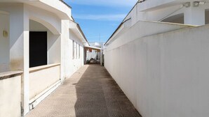 A narrow, paved alleyway between white buildings with a covered outdoor seating area at the end.