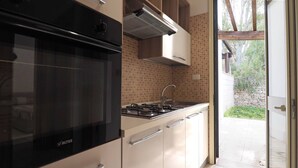 Een moderne keuken met een zwarte kookplaat, roestvrijstalen kastjes en uitzicht op de tuin door een glazen deur.