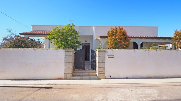 A two-story building with a white facade, a tiled roof, and a black gate. There are trees and shrubs in front of the building. - Villa Fede - 3 Bedrooms 2 Bathrooms air Conditioning by the sea (Taviano)