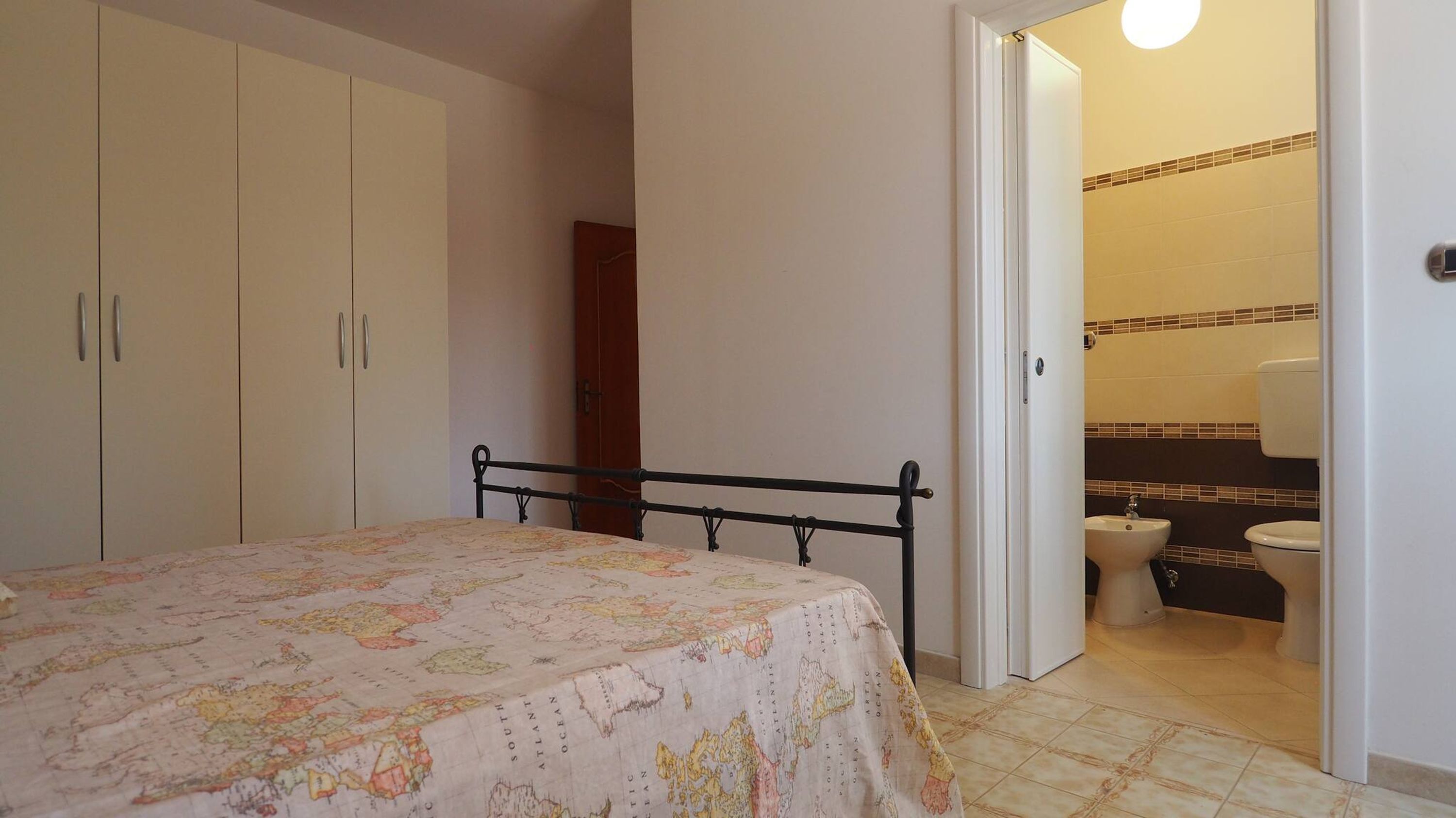 Ein Schlafzimmer mit Bett, Kleiderschrank und einem durch eine offene Tür einsehbaren Badezimmer.
