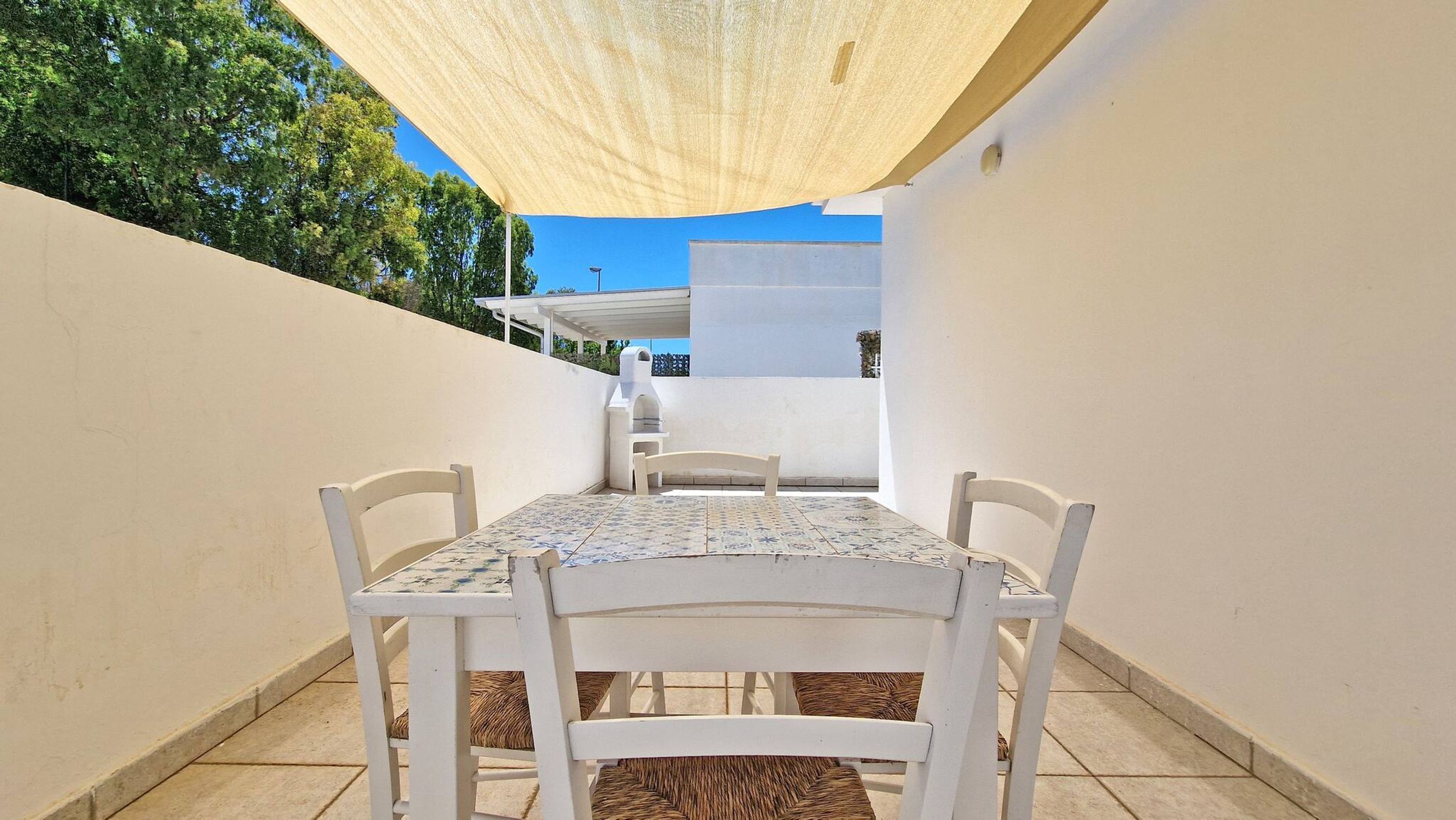 A patio with a table and chairs, a barbecue grill, and a white wall.
