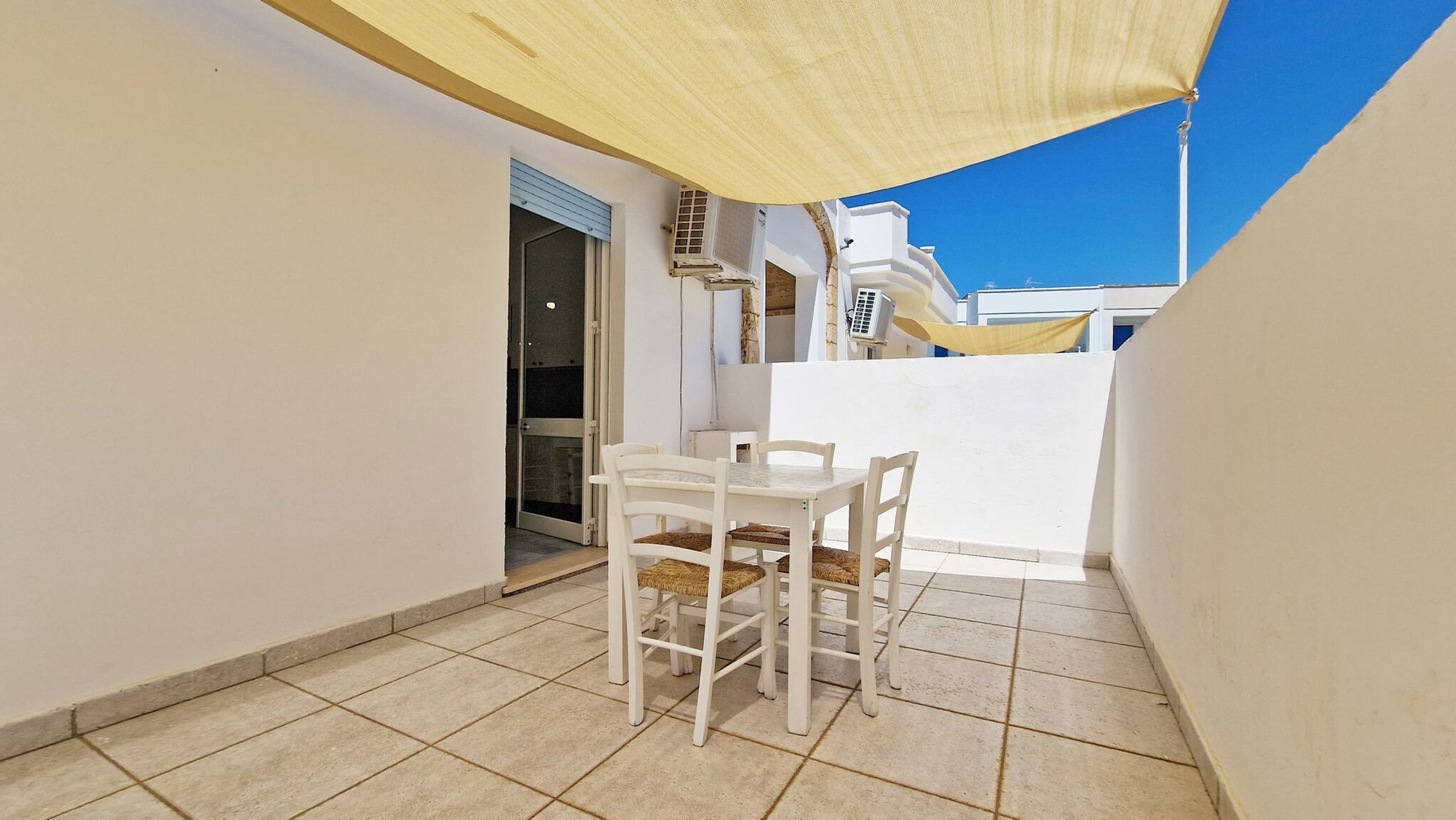 Une petite terrasse avec une table et des chaises, une porte et un auvent jaune.