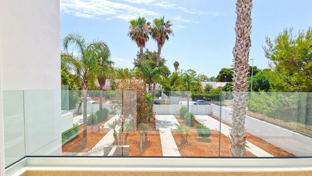 Un balcón con vistas a un jardín ajardinado, con palmeras y un sendero.