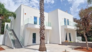 Un edificio moderno de dos pisos con una escalera que conduce a la entrada, un balcón de cristal y una palmera en primer plano.