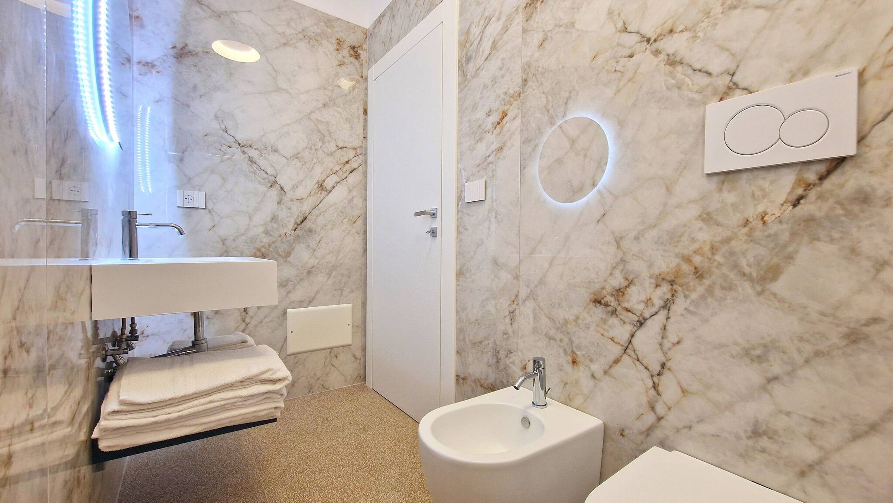 A modern bathroom with a marble backsplash, a sink, a bidet, and a towel rack.