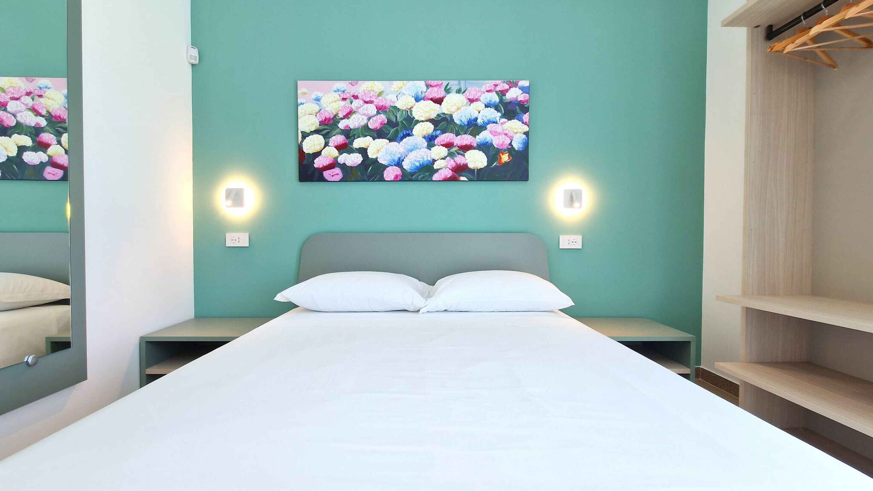 Ein modernes Schlafzimmer mit einem großen Bett, zwei Nachttischen, einem an der Wand hängenden Blumenbild und einem Holzschrank.