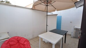 A small patio area with a white table, a red chair, and a beige umbrella providing shade. - Villa for 6 People 2 Bedrooms a few Meters From the sea (Ugento)