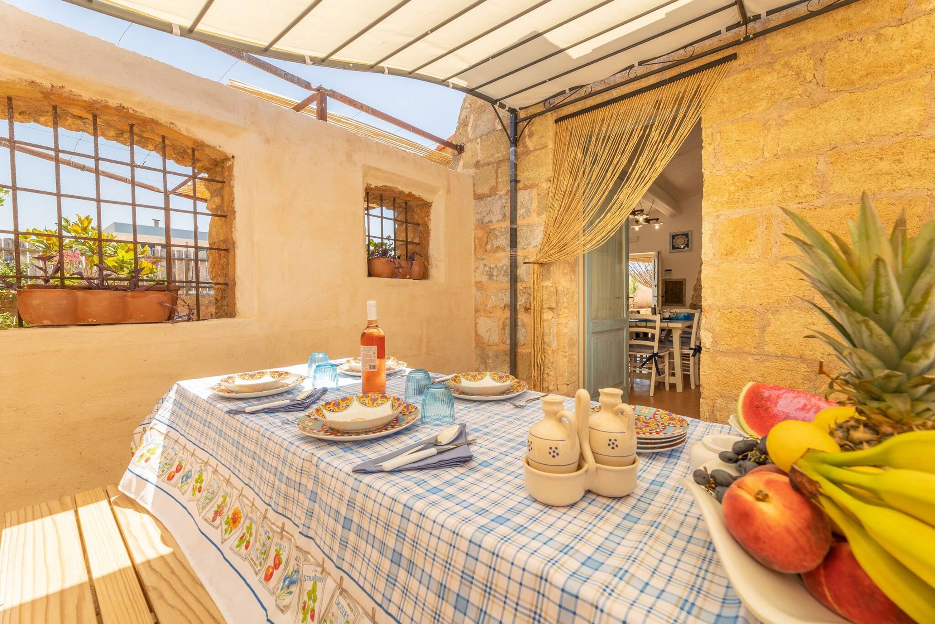 A dining area with a checkered tablecloth, potted plants, and a fruit platter.