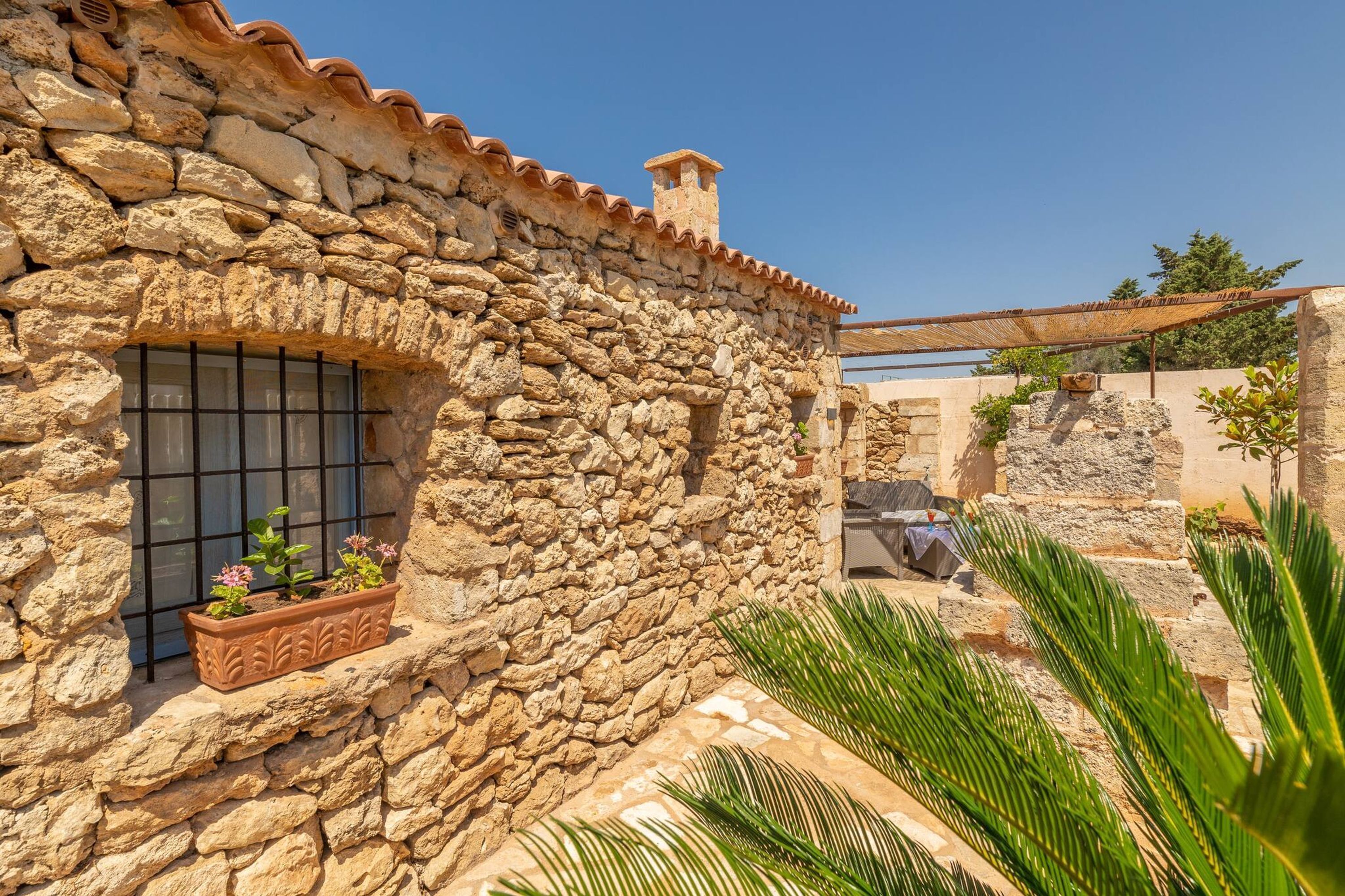 A stone building with a window, a small balcony, and a pergola.