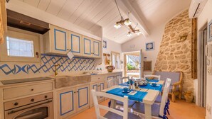 A kitchen with white cabinets, blue accents, a built-in oven, and a dining area with a table set for four. - Trullo Mmammineddhu in Torre San Giovanni (Ugento)