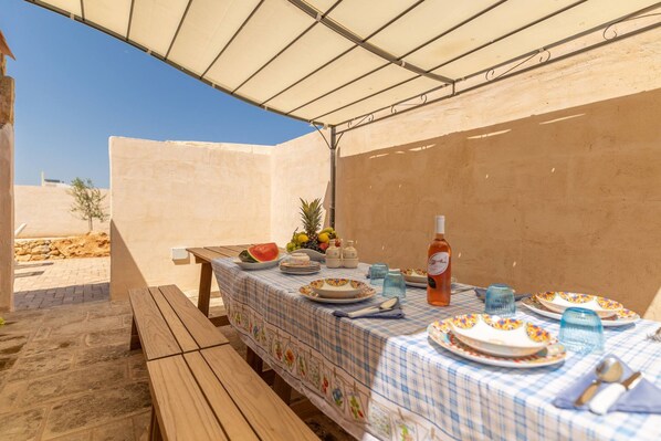 Un espace de restauration en plein air avec une table dressée pour quatre personnes, protégée par un auvent blanc.