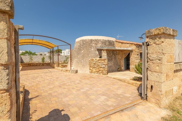 Un patio con muros de piedra, un área empavedada y una entrada cubierta.