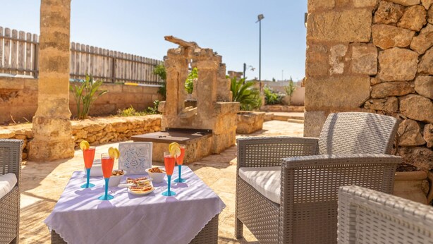 An outdoor patio with wicker furniture, a table set with drinks and snacks, and stone walls. - Trullo Mmammineddhu in Torre San Giovanni (Ugento)