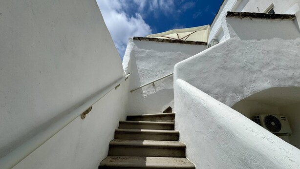 A white staircase with a handrail leading to a room with a window and an air conditioning unit. - App al Castello 2 by Salentoaffitti (Alliste)