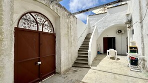 A narrow courtyard with a brown gate, a staircase leading to a door, and a small table with chairs. - App al Castello 2 by Salentoaffitti (Alliste)