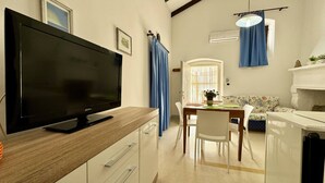 A modern living room with a flat-screen TV on a wooden cabinet, a dining area with a table and chairs, a sofa, and a fireplace. - App al Castello 2 by Salentoaffitti (Alliste)