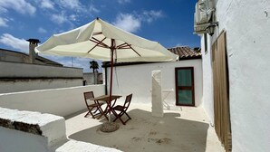 A small patio with a table and chairs, an umbrella, and a white wall. - App al Castello 2 by Salentoaffitti (Alliste)