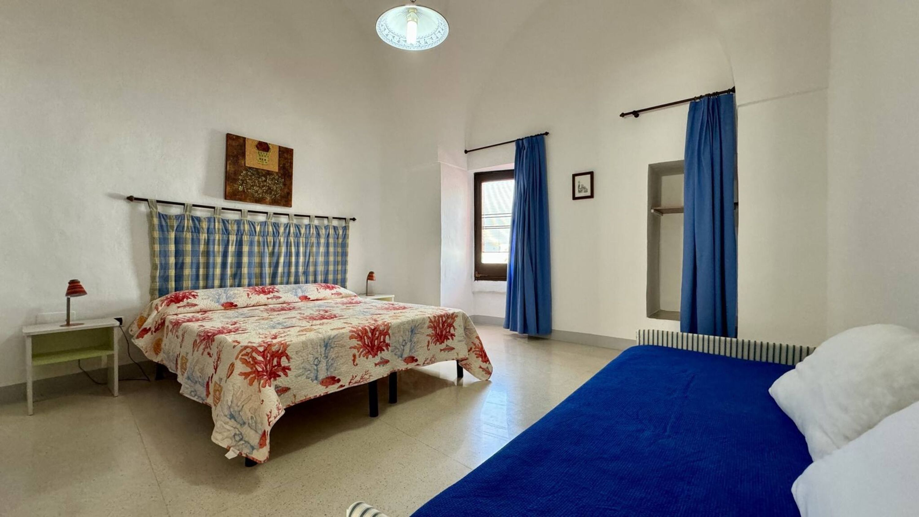 A bedroom with a bed, a nightstand, a radiator, and a window with curtains.