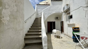 A narrow staircase leading to a door, a small outdoor seating area with a table and chairs, and a trash bin. - App al Castello 2 by Salentoaffitti (Alliste)