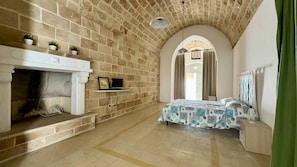 A bedroom with a stone fireplace, a bed with a patterned bedspread, and an arched doorway. - App al Castello 1 by Salentoaffitti (Alliste)