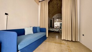 A room with a blue sofa, a dining area with a table and chairs, and a stone wall. - App al Castello 1 by Salentoaffitti (Alliste)