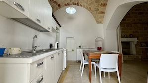 A compact kitchen with white cabinetry, a sink, and a dining area with a table and chairs. - App al Castello 1 by Salentoaffitti (Alliste)