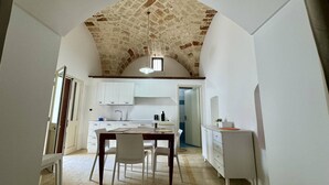 A narrow, vaulted room with a kitchen area, white cabinetry, and a dining table with chairs. - App al Castello 1 by Salentoaffitti (Alliste)