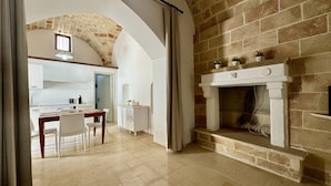 A modern kitchen with a stone fireplace, a dining area with a table and chairs, and an arched stone ceiling. - App al Castello 1 by Salentoaffitti (Alliste)