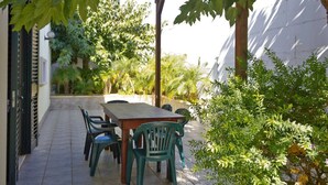 Eine Terrasse im Freien mit Tisch und Stühlen, umgeben von üppiger Vegetation und einem weißen Gebäude im Hintergrund.