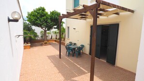 A covered patio with a table and chairs, a wooden pergola, and a door. - Appartamento Torre Suda 1 (Racale)