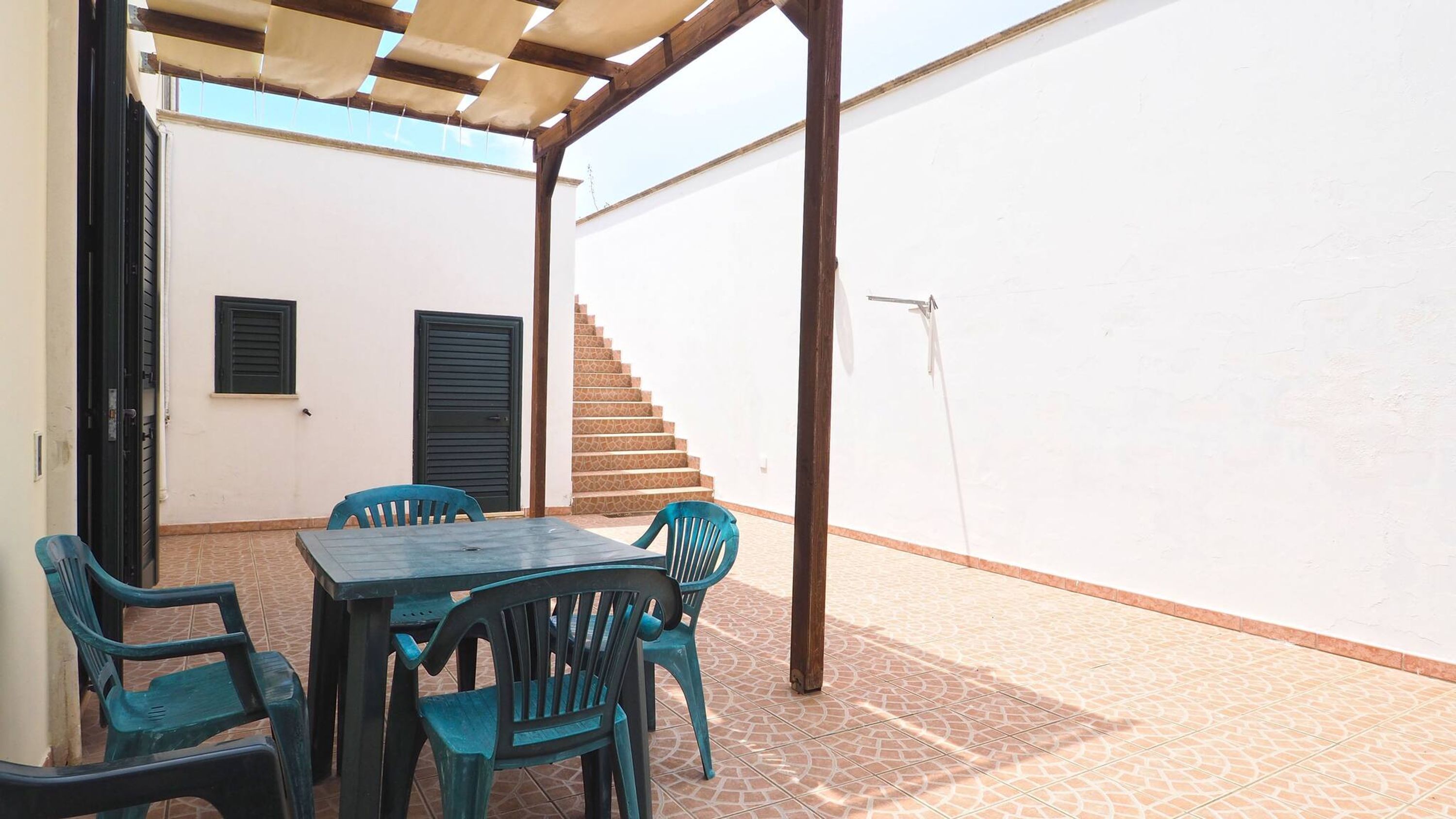 A covered patio with a table and chairs, a staircase, and a white wall.