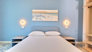 Un dormitorio con una cama, dos mesitas de noche y un cuadro de una playa.